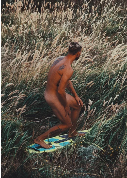 A nude man posing on a surfboard